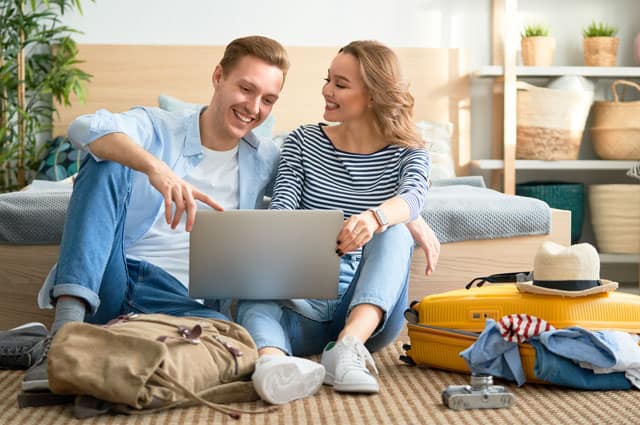 Vera Birkenbihl Online Sprachkurs Urlaub Reisevorbereitung | Klarsicht Verlag Ein junges Paar sitzt zuhause auf dem Boden, die gepackten Koffer neben ihnen und sie planen freudig die bevorstehende Reise.