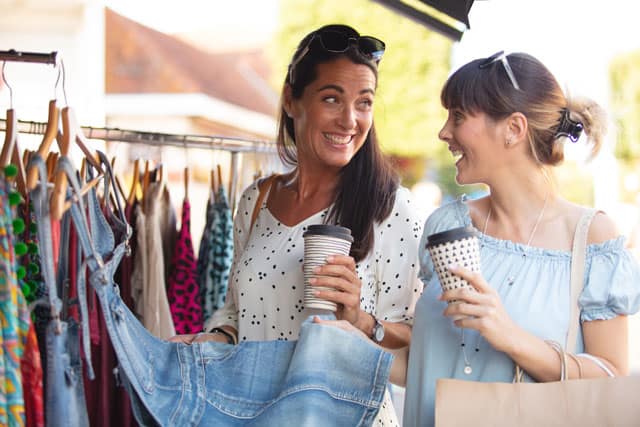 Vera Birkenbihl Online Sprachkurs Urlaub Shoppen | Klarsicht Verlag Zwei Frauen haben an einem sonnigen Tag Spass beim Shoppen und schauen sich gemeinsam Kleidung an.