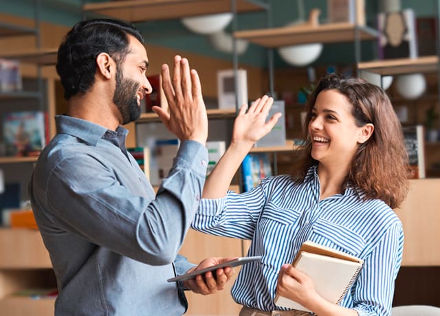 Vera Birkenbihl Online Sprachkurs Fortgeschrittene Team | Klarsicht-Verlag Ein Mann und eine Frau lachen sich zufrieden an und geben sich ein High Five mit den Haenden.